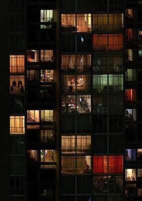 Vista de um prédio por fora, está de noite e as casas têm a luz ligada.